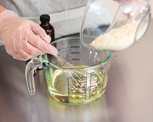 skin soothing balm being mixed, image shows wax being added to oil being mixed with a wisk